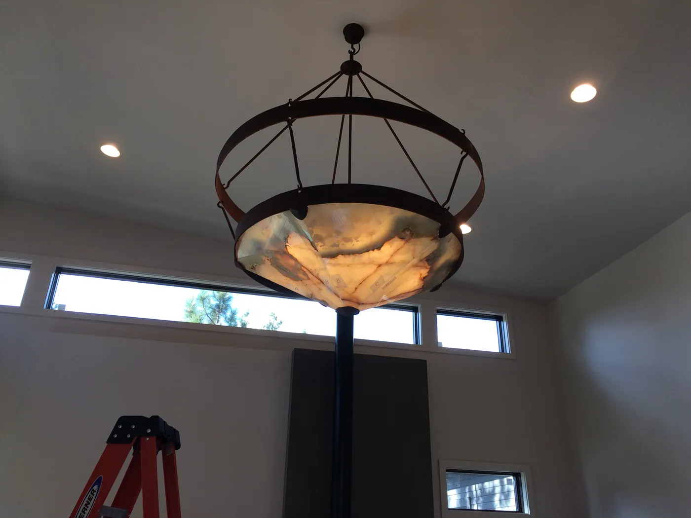 A round alabaster chandelier hanging in a room with high windows