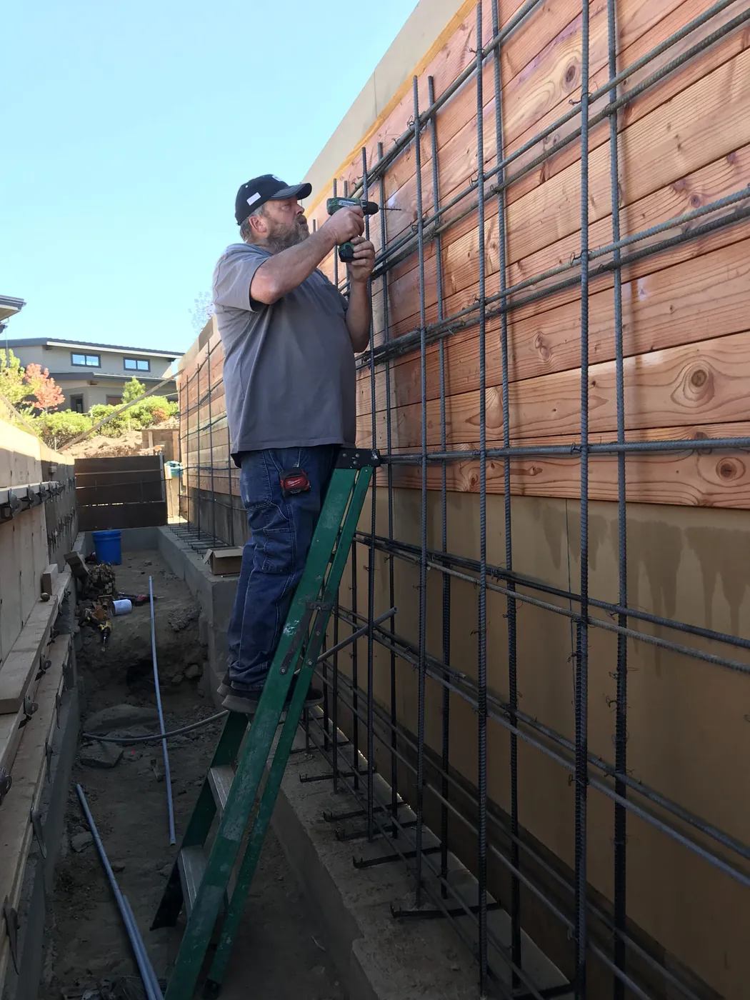 An electrician on a ladder at a concrete wall form with rebar