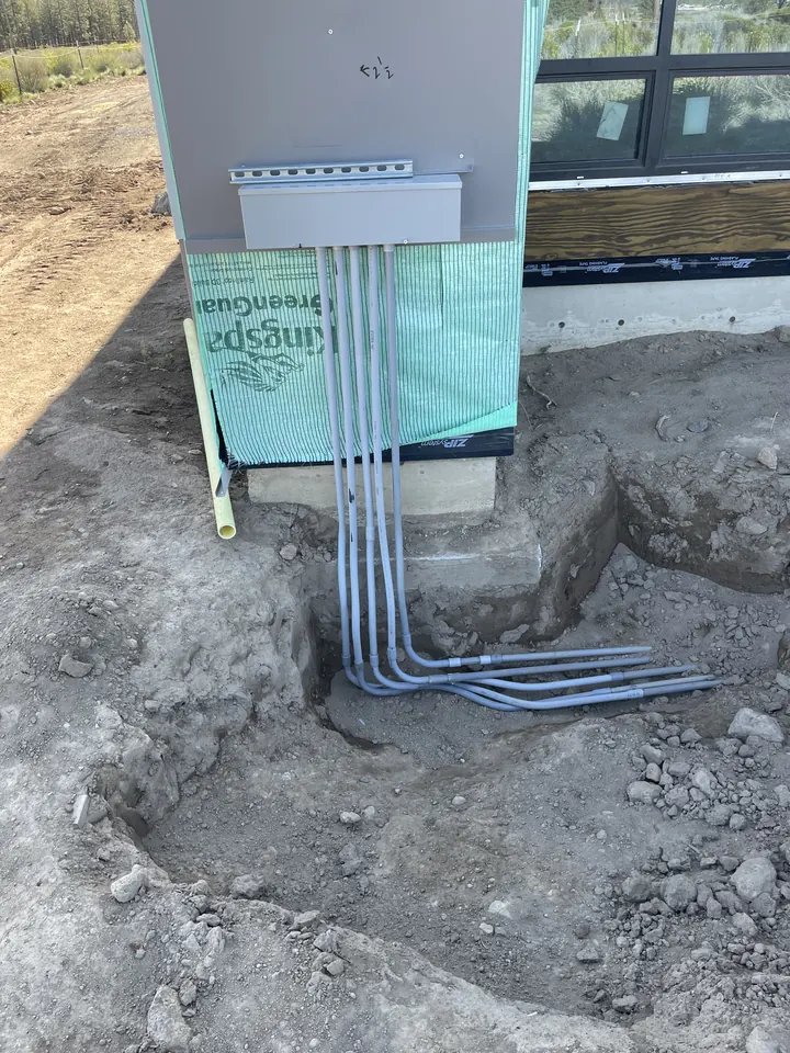 Gray conduit runs coming up out of a trench into a building