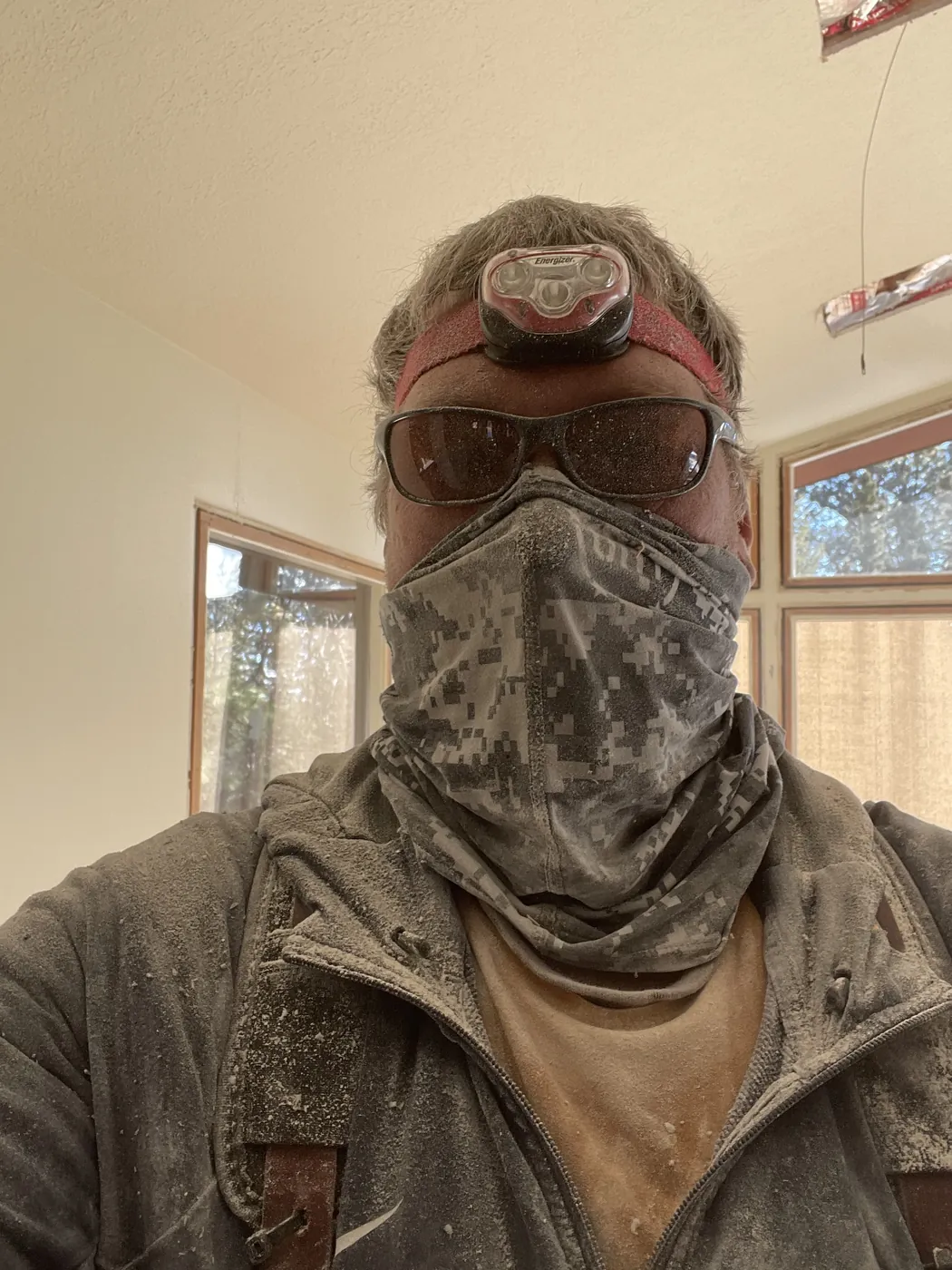 An electrician covered in drywall dust after a bath fan installation