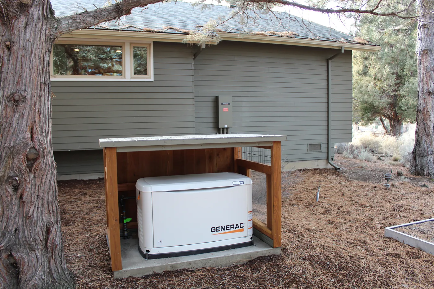 A standby generator in a cedar enclosure beside a home, under pines