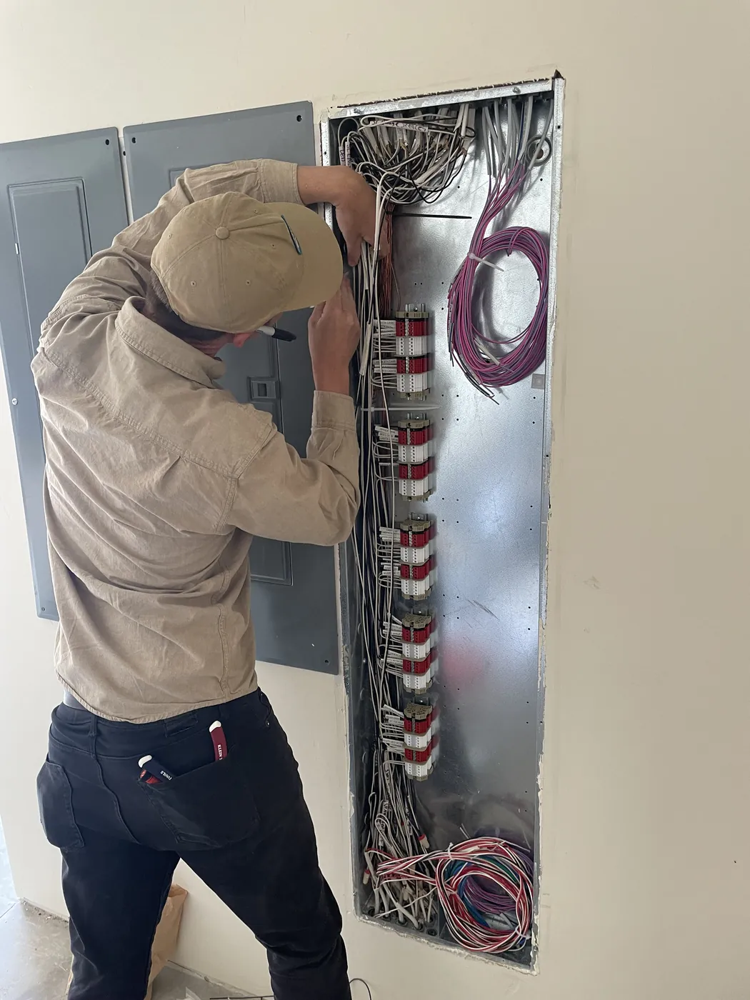 An electrician working inside a tall lighting panel full of colored wire