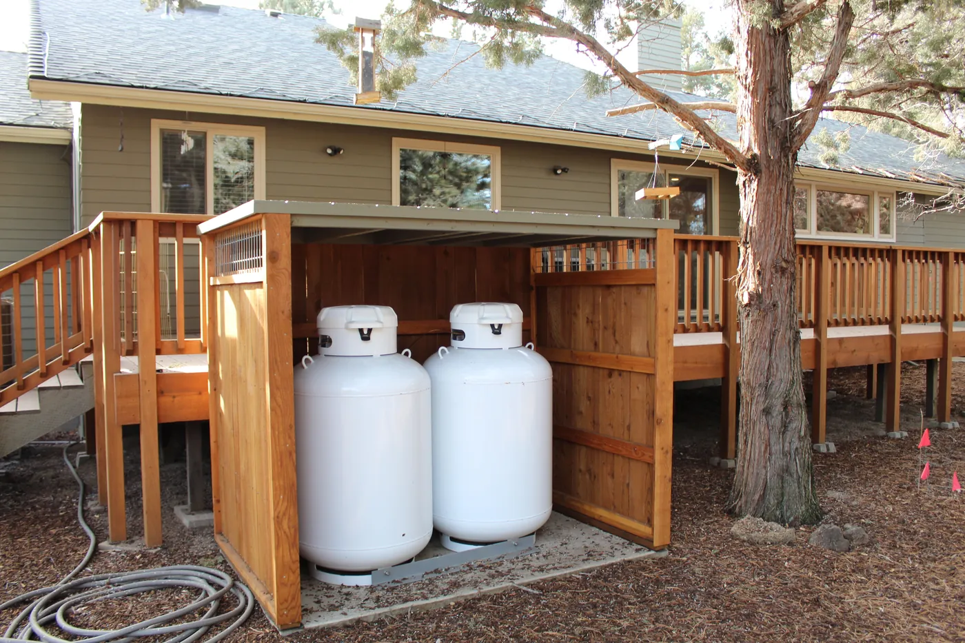 Two propane tanks in a cedar enclosure beside a deck
